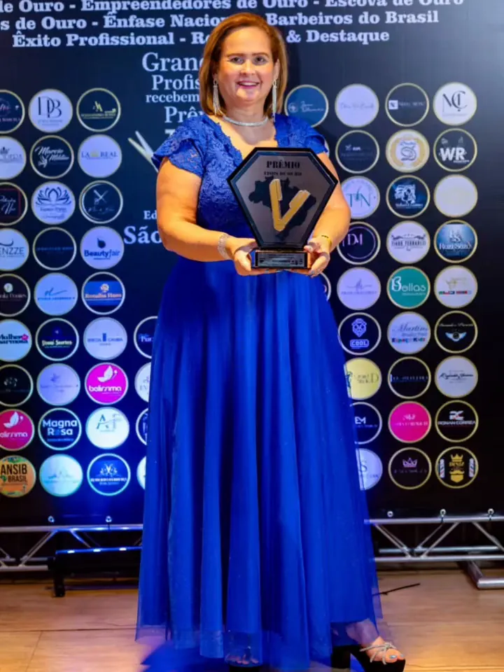 Fátima Alves Santos de vestido azul segurando o troféu do Prêmio Tesoura de Ouro